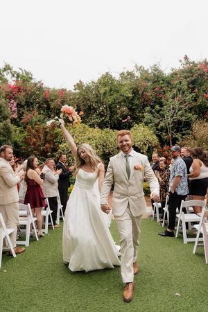 Wedding guests celebrate joyfully during an outdoor garden ceremony with white chairs on green lawn.
