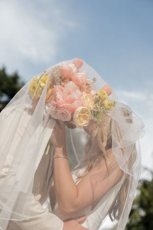 Dreamy close-up of a bridal bouquet with peach and yellow flowers through flowing veil.