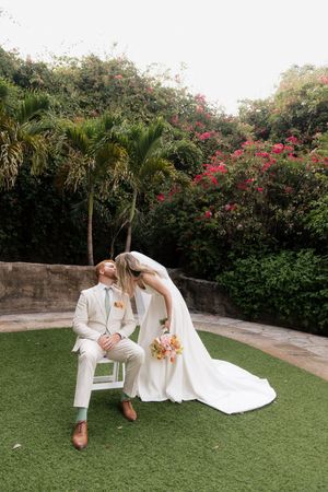 A romantic wedding moment captured in a tropical garden setting with palm trees and pink bougainvillea flowers.