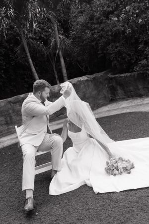 Black and white photo of couple in playful wedding pose on grass.