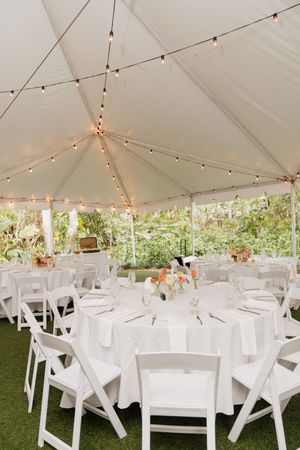 Elegant wedding reception setup under a white tent with string lights and round tables with white linens.
