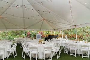 An elegant white tent reception setup with string lights and round tables for a garden wedding.