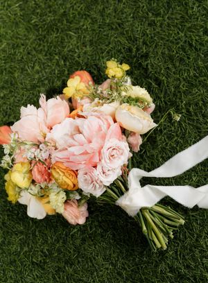 Beautiful pink and peach bridal bouquet lying on green grass.