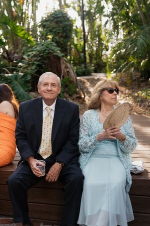 Wedding guests enjoying a casual moment on wooden benches in a lush tropical garden setting.