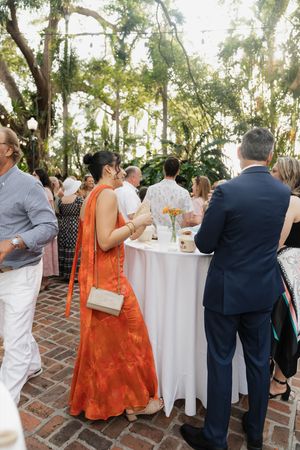 Wedding reception guests mingling around cocktail tables under trees.