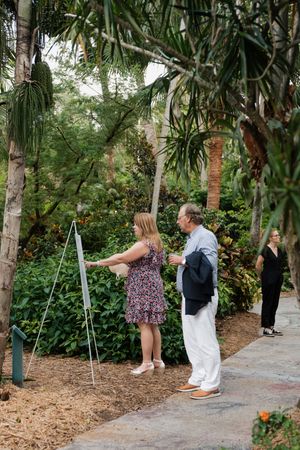 Wedding guests explore a lush tropical garden path lined with palm trees and greenery during an outdoor celebration.
