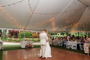 Wedding reception tent decorated with string lights and white chairs set up for dinner celebration.