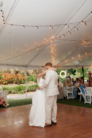 Couple shares romantic first dance under twinkling lights at outdoor wedding reception.