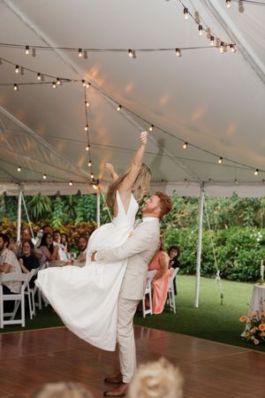 A couple performs a dramatic dance lift under a tent with string lights at their wedding reception.