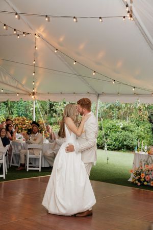 A couple shares their first dance under a white tent decorated with string lights at an outdoor wedding reception.
