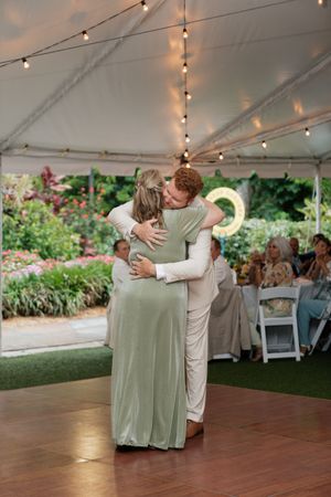 Newlyweds perform romantic dance moves on wooden floor under tent with string lights.