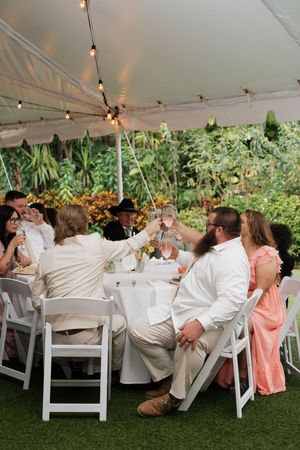 Wedding guests seated at long tables under a white tent during an outdoor reception celebration.