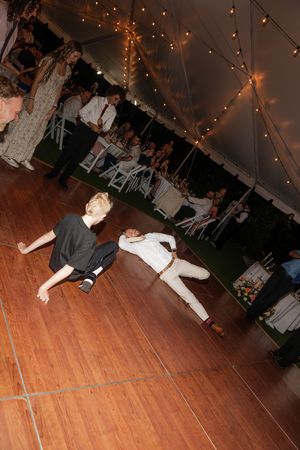 Two dancers performing energetic moves on a wooden dance floor under twinkling lights at an evening reception.
