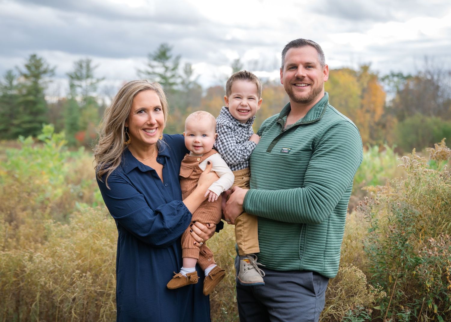 A family in coordinated white and blue outfits poses together in a pine forest setting.