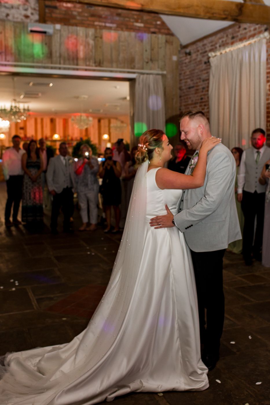 A couple shares a slow dance on their wedding day in a rustic venue with exposed brick walls and mood lighting.
