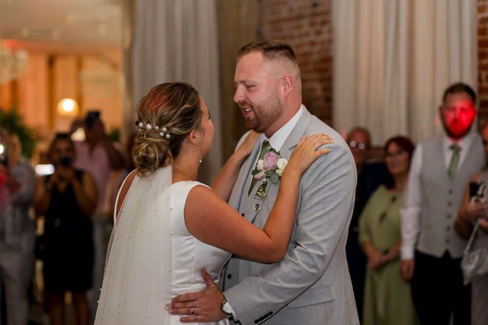 Wedding couple dances together in a romantic moment at their reception with guests watching in the background.