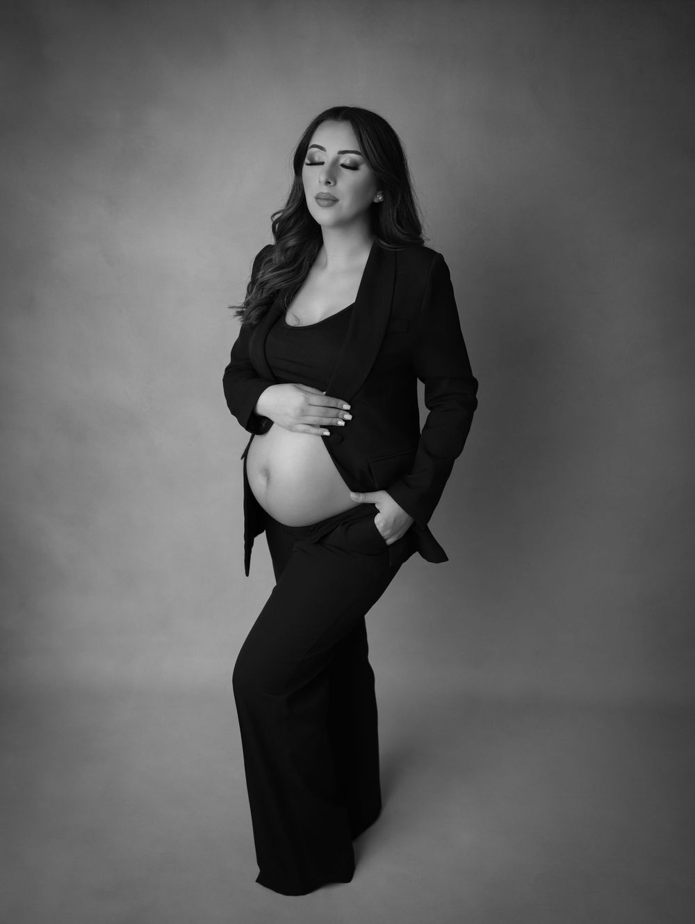 A black and white maternity portrait featuring a classic business suit look.