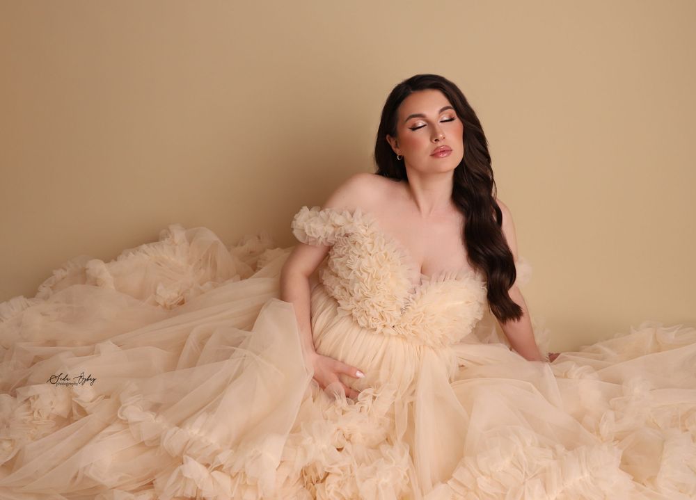 Flowing champagne-colored maternity dress captured in a warm studio setting with soft lighting.