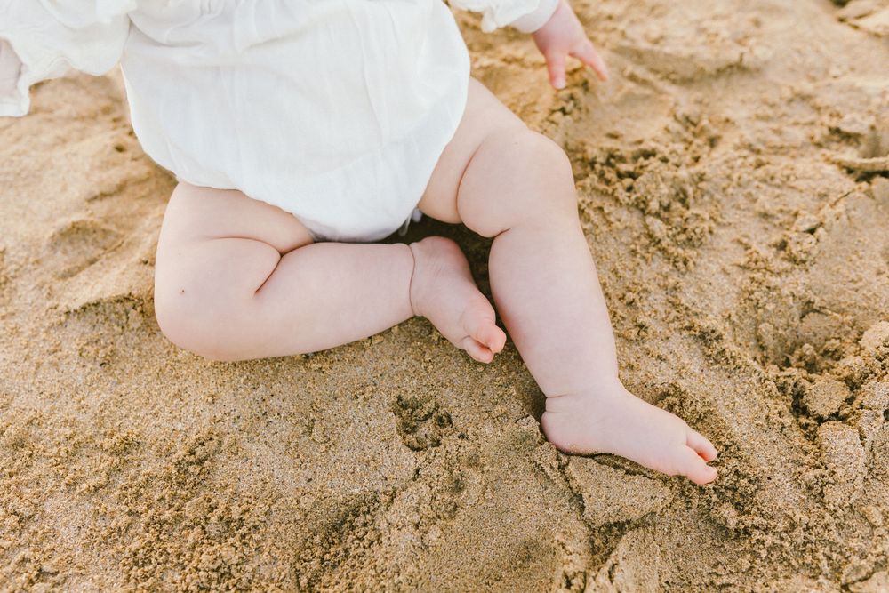 Close-up view of tiny baby feet resting on warm sandy beach.