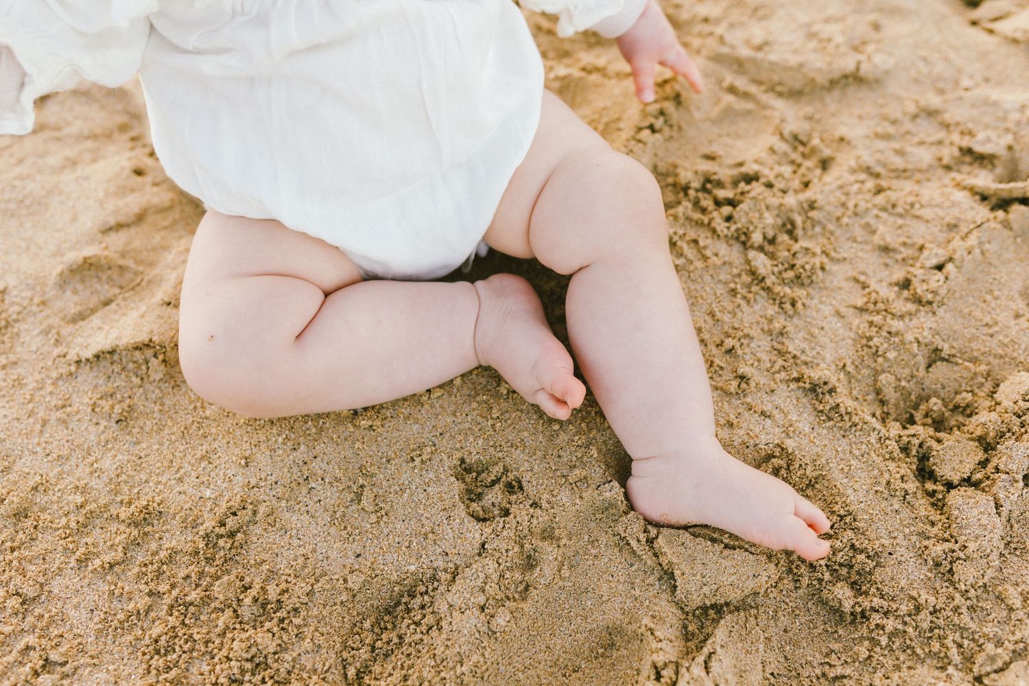 Close-up view of tiny baby feet resting on warm sandy beach.