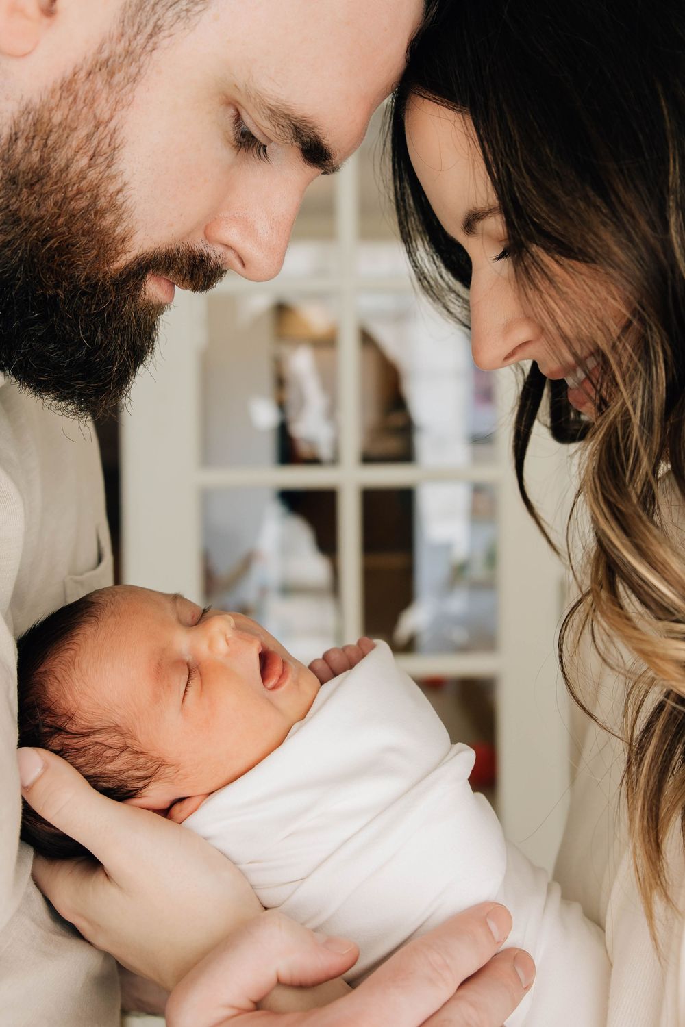 New parents lean in closely to gaze at their swaddled sleeping newborn baby with love.