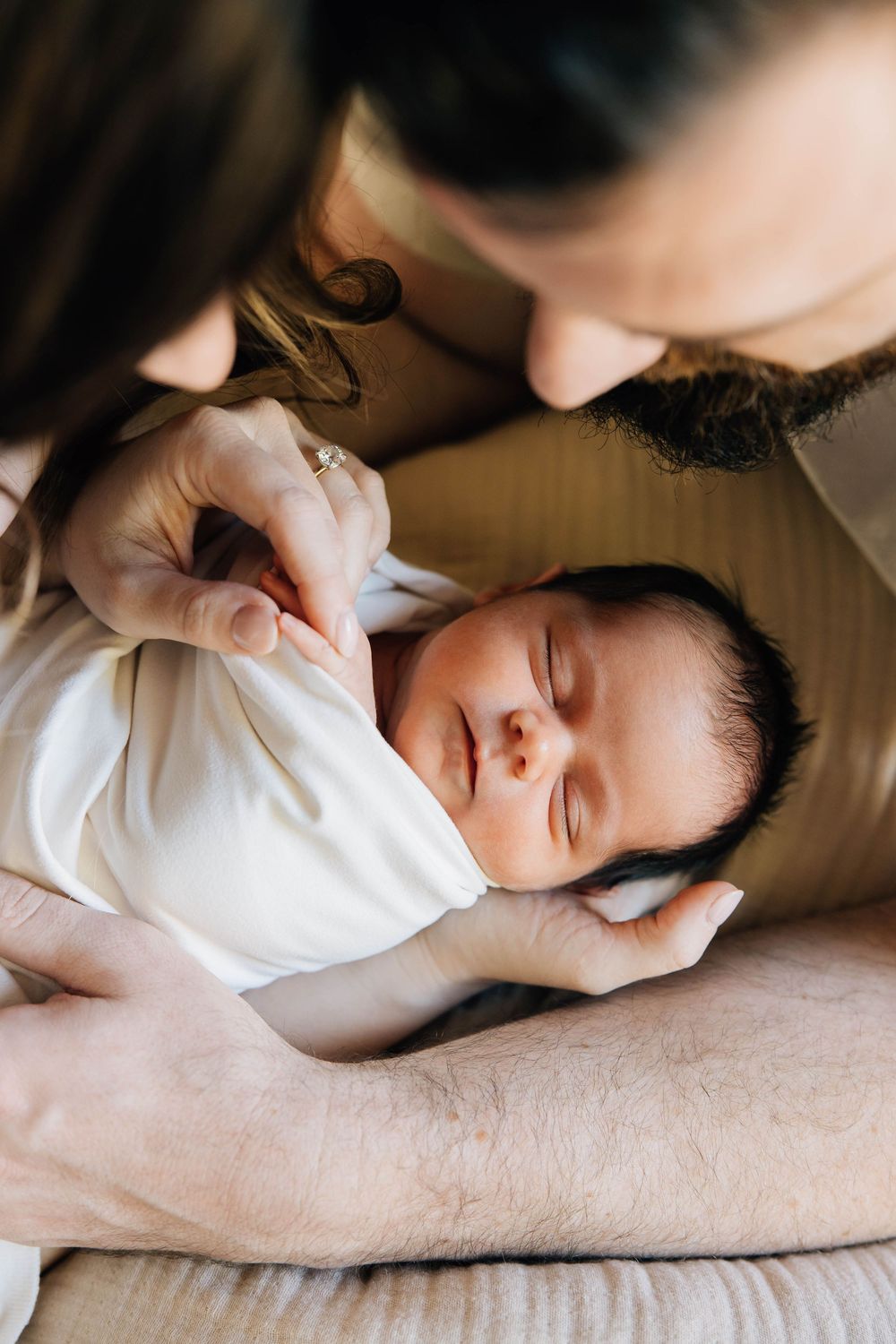 Parents lovingly gazing at peaceful sleeping newborn baby wrapped in white swaddle.