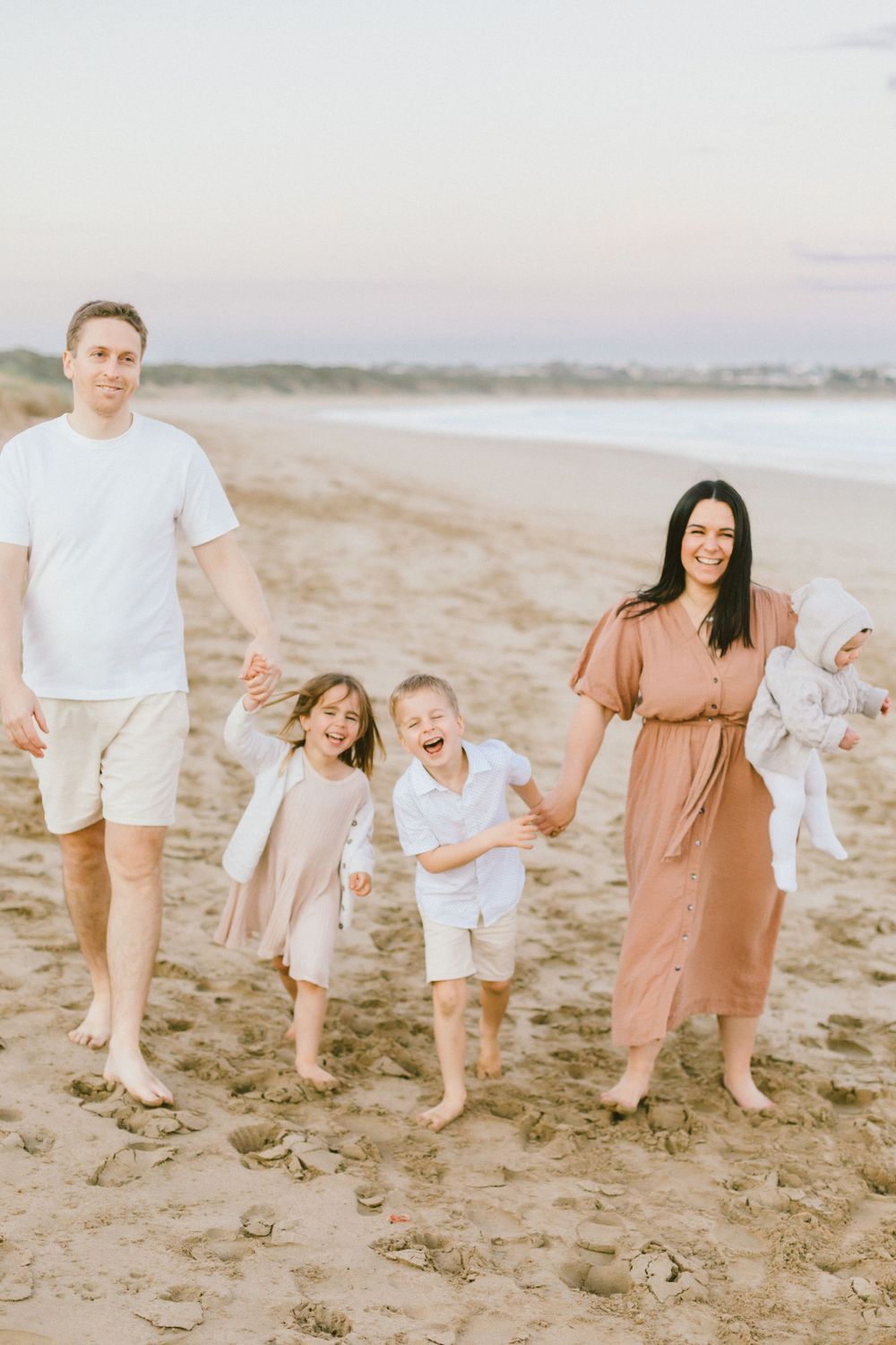 A family walking and playing together on a sandy beach at sunset with soft pastel colors in the background.