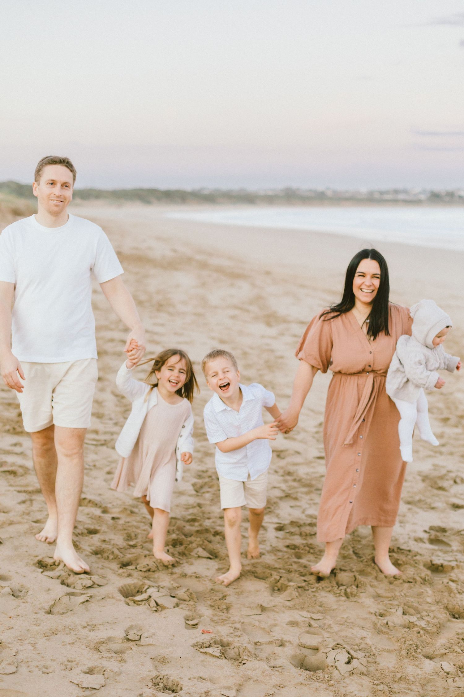 A family walking and playing together on a sandy beach at sunset with soft pastel colors in the background.