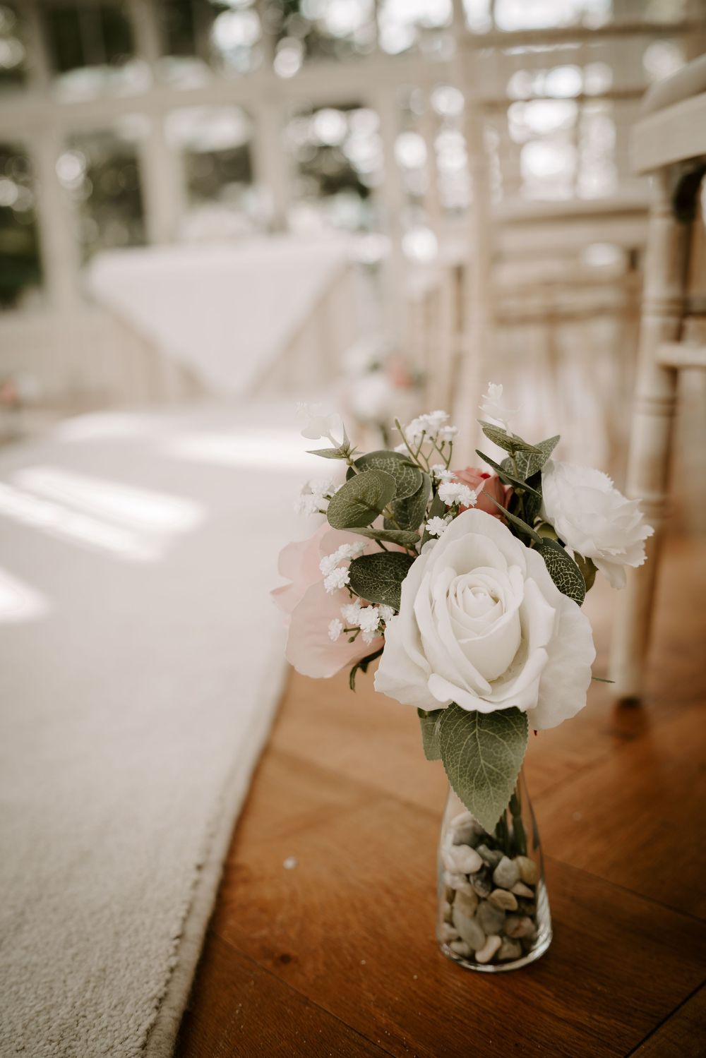 Delicate white roses and greenery arranged in small glass vases on a wooden surface.