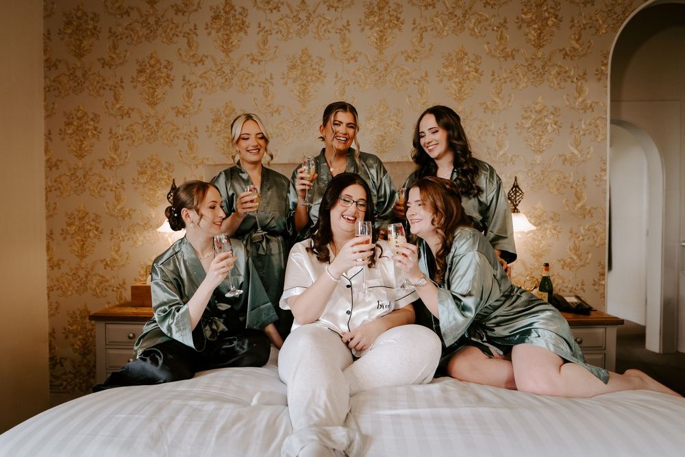 Wedding party in matching robes celebrates on a bed during pre-ceremony preparations.