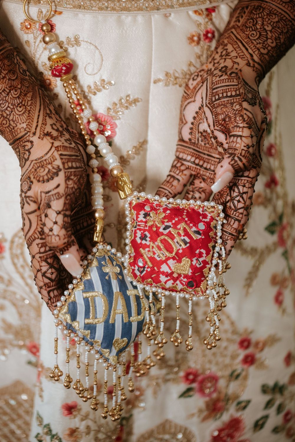 Intricate henna-adorned hands holding colorful decorative objects against a floral patterned background.