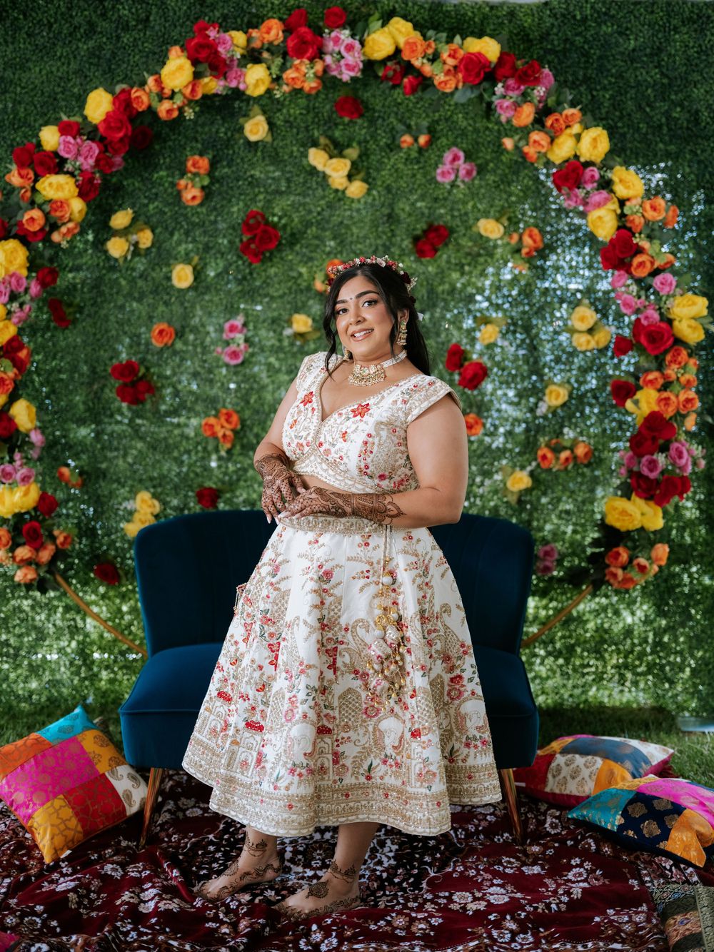 Colorful floral arch with red, yellow and pink blooms creates a vibrant backdrop against lush green foliage.