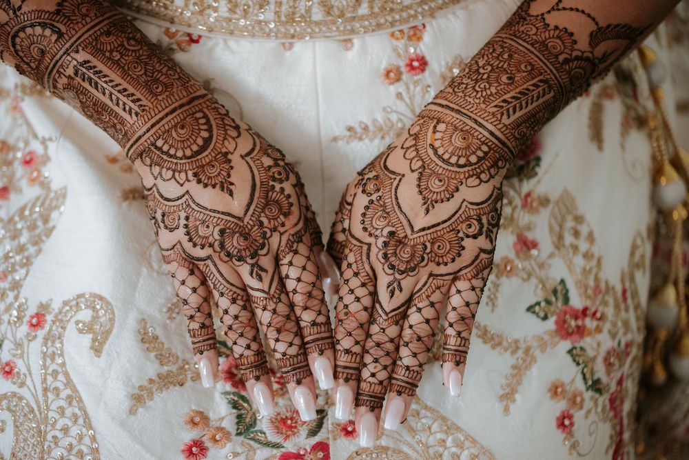 Intricate henna mehndi designs adorn hands with delicate floral and paisley patterns against a floral fabric background.