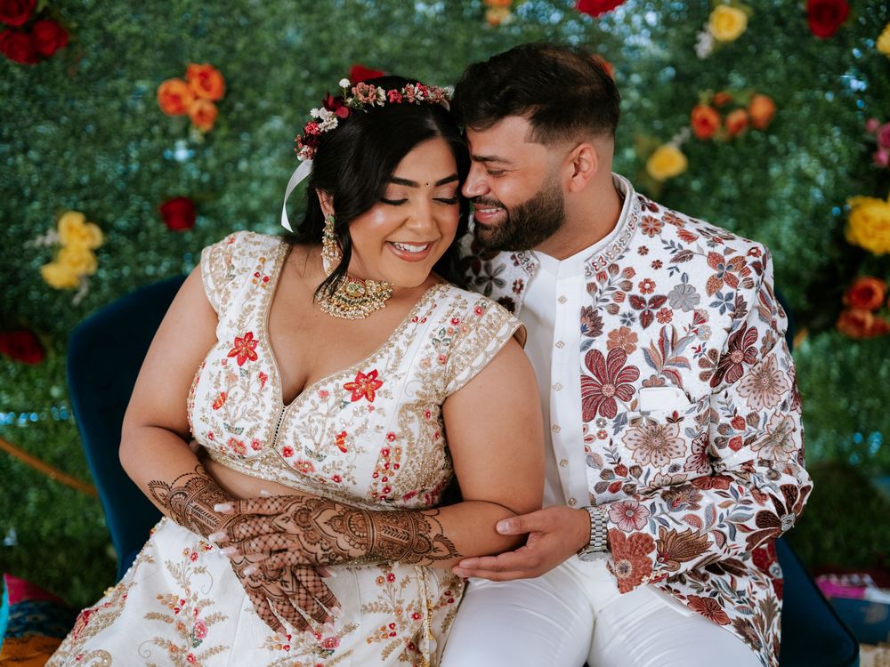 A couple in matching floral outfits embraces lovingly in a garden filled with vibrant red and orange flowers.