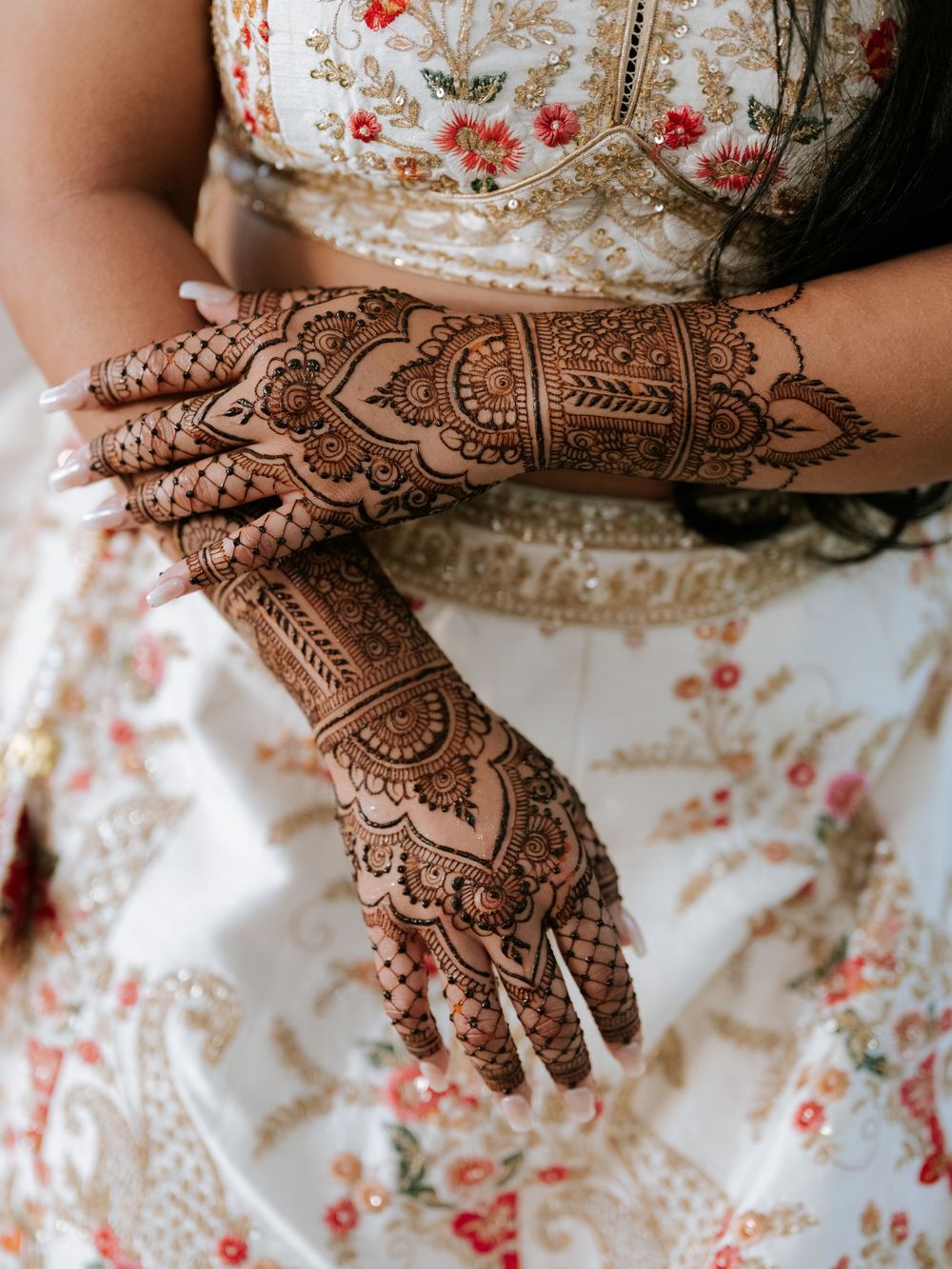 Close-up view of intricate henna designs on hands against a floral print dress background.