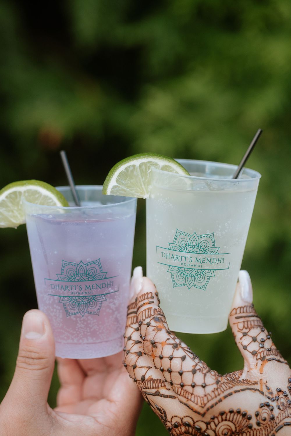 Two frosted glasses with citrus garnish clink together in a celebratory toast against a blurred green background.