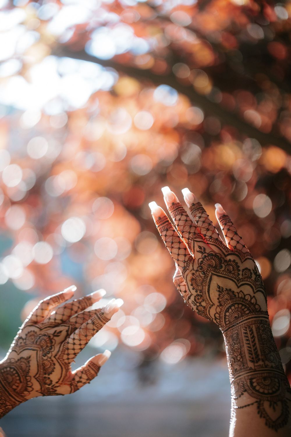 Beautiful henna design on hands shown against blurred autumn bokeh background with warm orange tones.