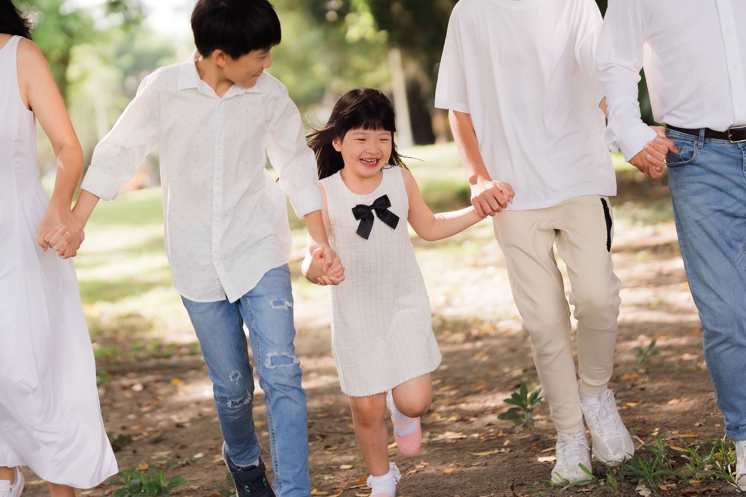 A group of people in white clothing walk together through a sunlit outdoor path in a casual summer setting.