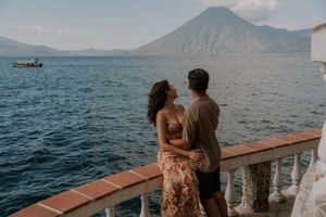 Couple embracing on a lakeside terrace with a volcanic mountain and boat on the water in the background.