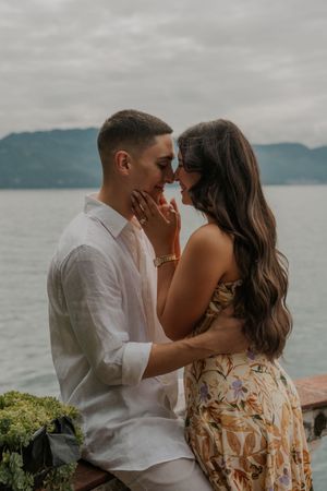 A romantic couple shares intimate moments by a scenic lake with mountains in the background.