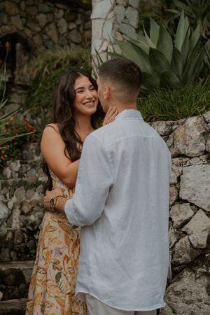 A couple shares intimate moments against a stone wall backdrop in a romantic outdoor setting.