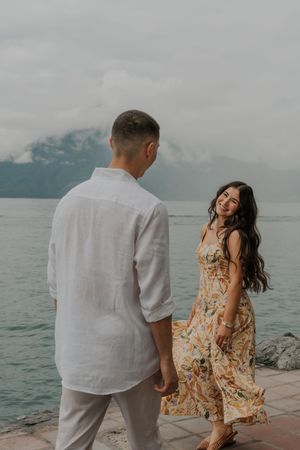 A couple shares romantic moments by the ocean with cloudy skies and turquoise waters in the background.