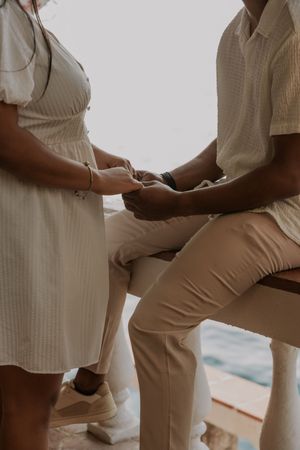 Couple holding hands while seated, wearing neutral tones, during an intimate outdoor ceremony.