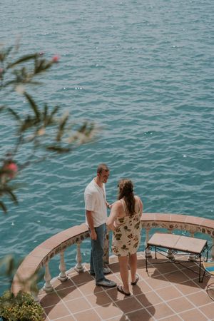A couple shares a romantic moment on a tiled terrace overlooking turquoise Mediterranean waters.