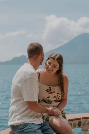 A couple shares intimate moments by a scenic lake with mountains in the background.