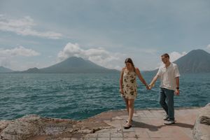 Couple walking hand in hand along coastal path with mountain and ocean views in scenic landscape setting.