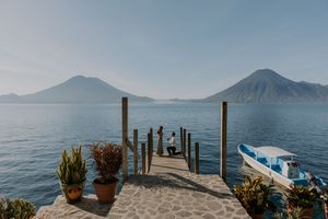 Wooden dock with potted plants extends into Lake Atitlan with volcanic mountains and calm waters in Guatemala.