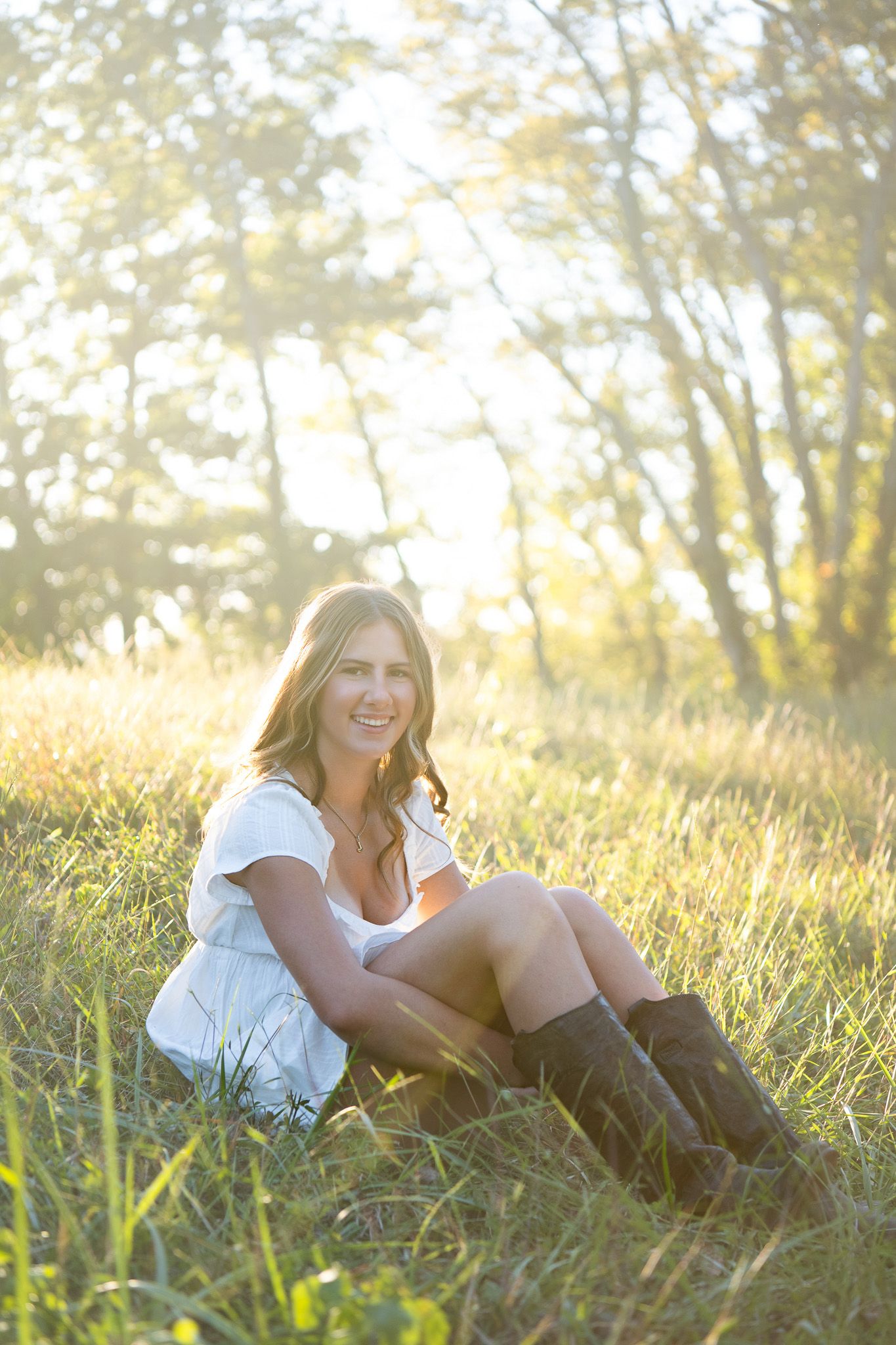 Person in a white top and boots relaxes in tall grass during golden hour sunset lighting.