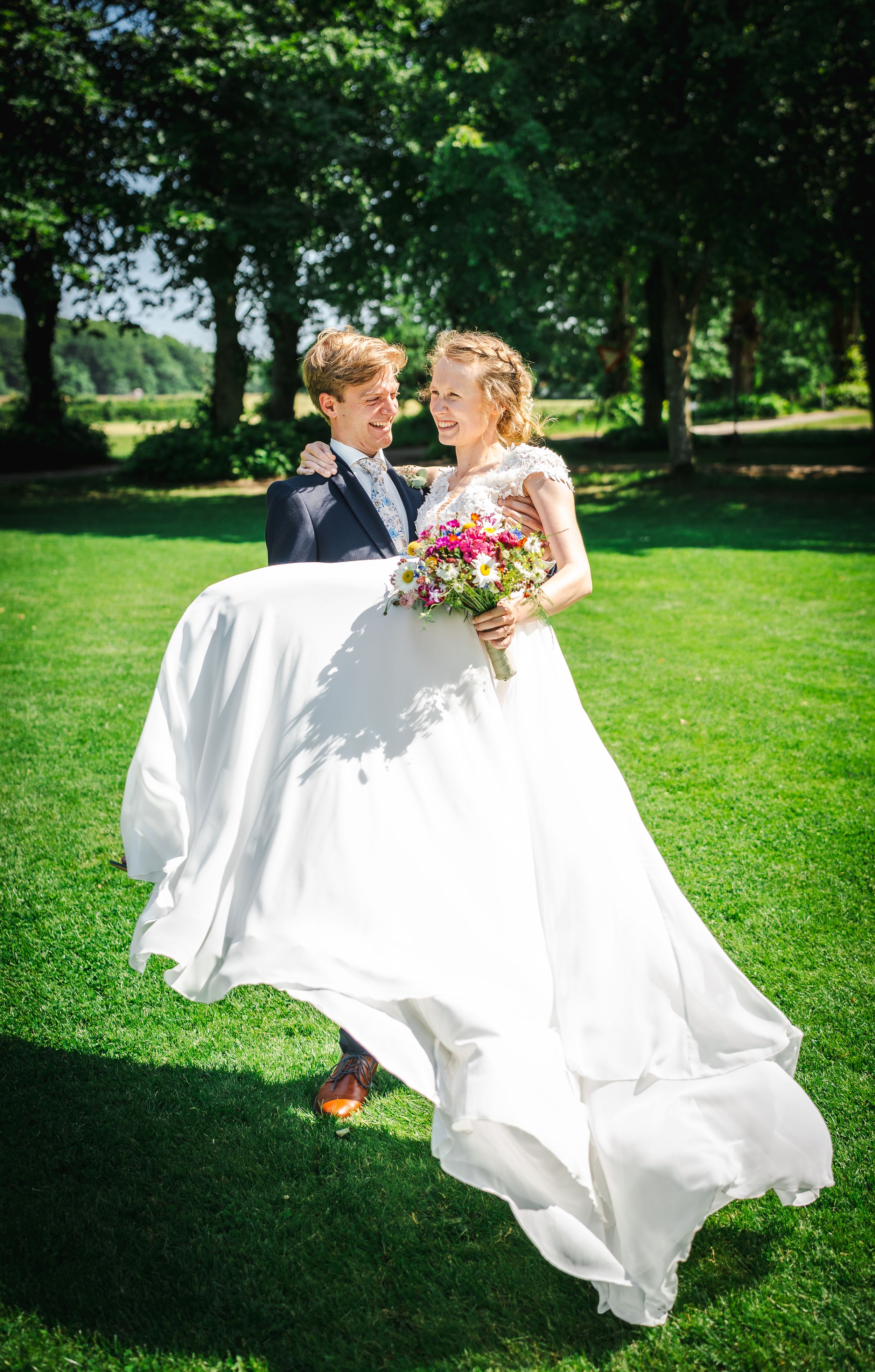 A romantic wedding couple dances in a sunlit garden as the bride's white dress flows elegantly in the breeze.