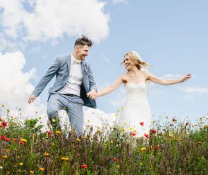 A couple dances together in a vibrant field of red poppies and wildflowers against a bright blue summer sky.